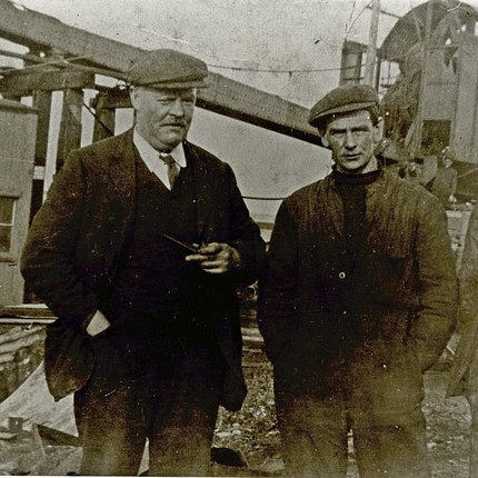 Two men standing in front of a steam crane
